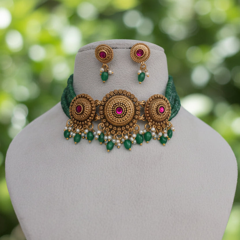 Gold and green traditional Indian jewelry set featuring a choker necklace and matching earrings, displayed on a cream-colored mannequin bust against a draped white fabric background.