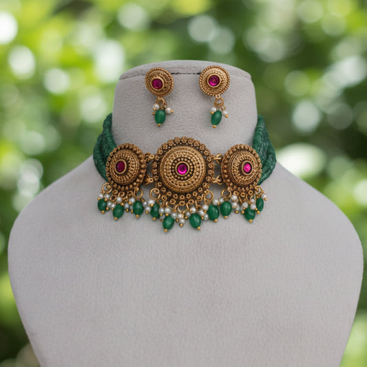 Gold and green traditional Indian jewelry set featuring a choker necklace and matching earrings, displayed on a cream-colored mannequin bust against a draped white fabric background.